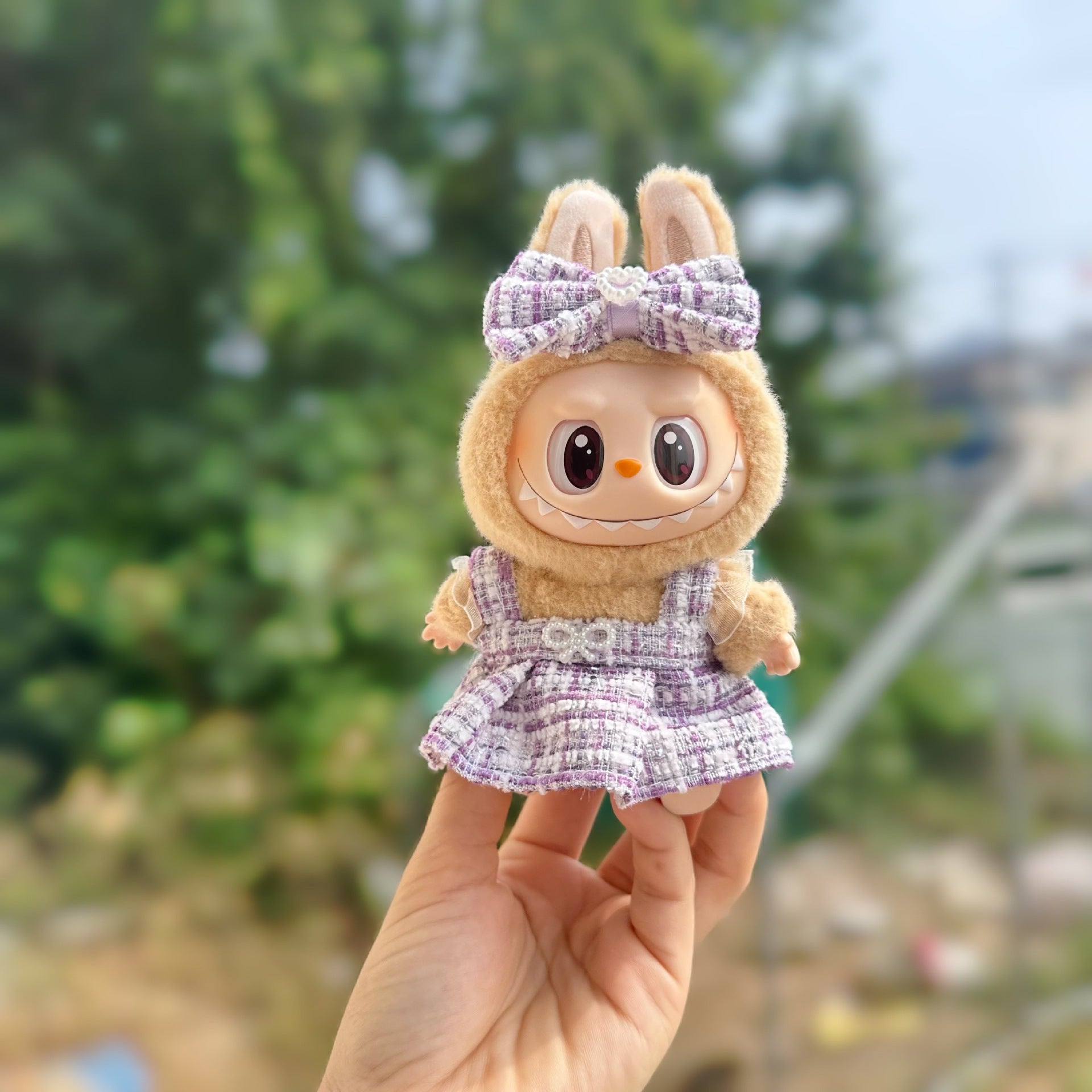 Small plush toy with a bow and dress held in a hand against a blurred outdoor background