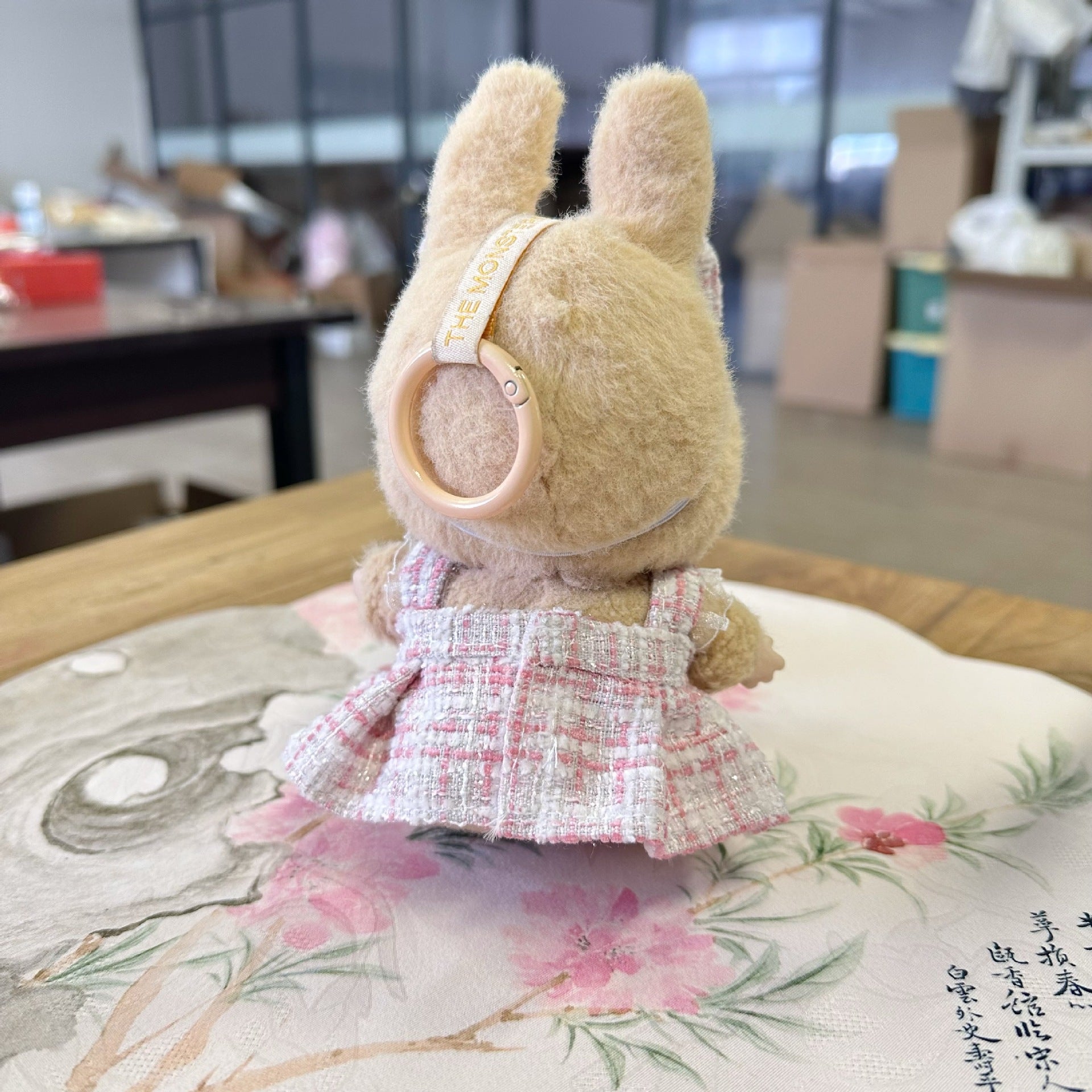 Stuffed animal toy with goggles and a dress on a floral cushion in an indoor setting