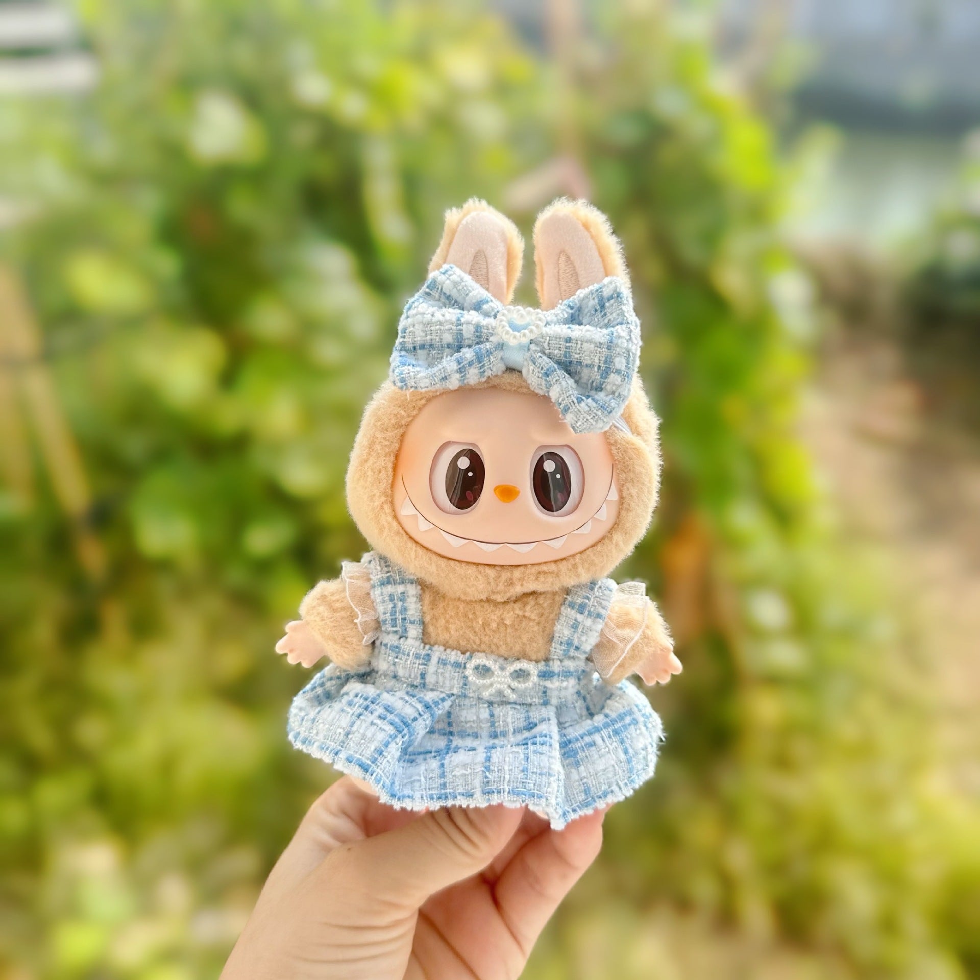 Toy figure of a rabbit in a blue dress with a bow held against a blurred green background
