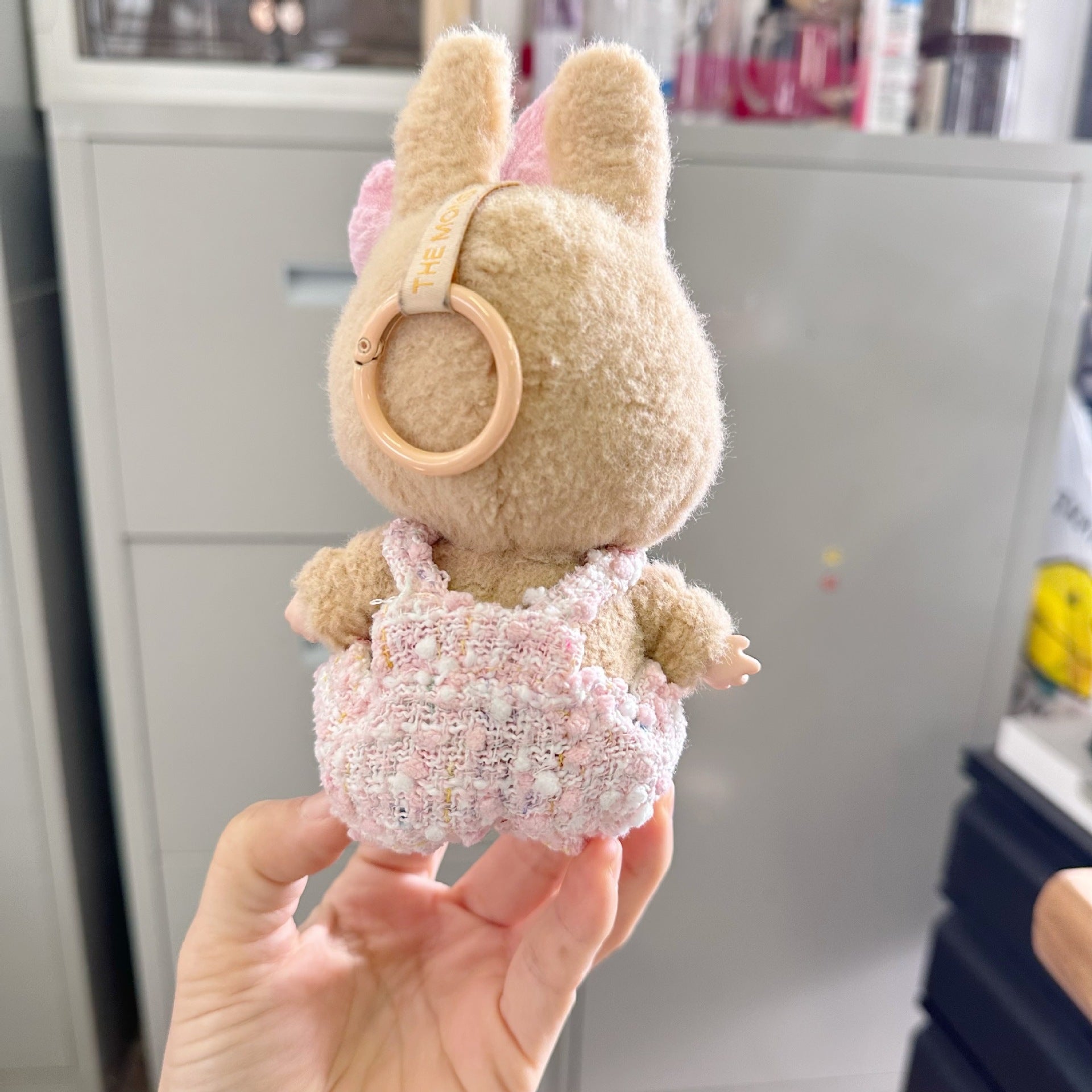Plush toy with bunny ears held in a hand against a blurred indoor background