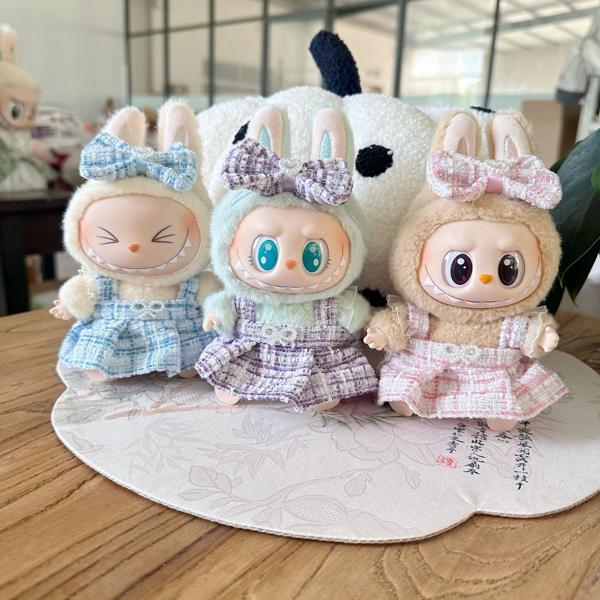 Three cute plush toys with bunny ears and colorful bows on a wooden surface.