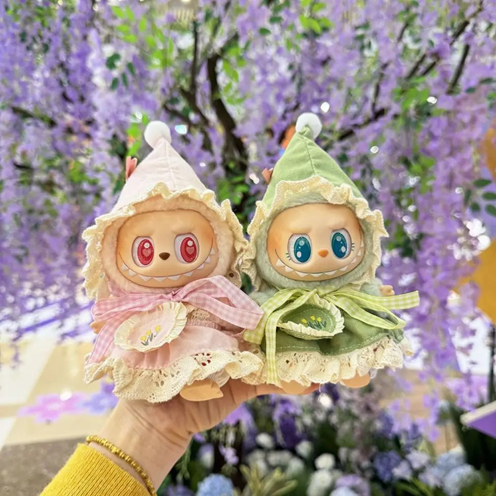 Two small plush toys with colorful dresses held against a backdrop of purple flowers.
