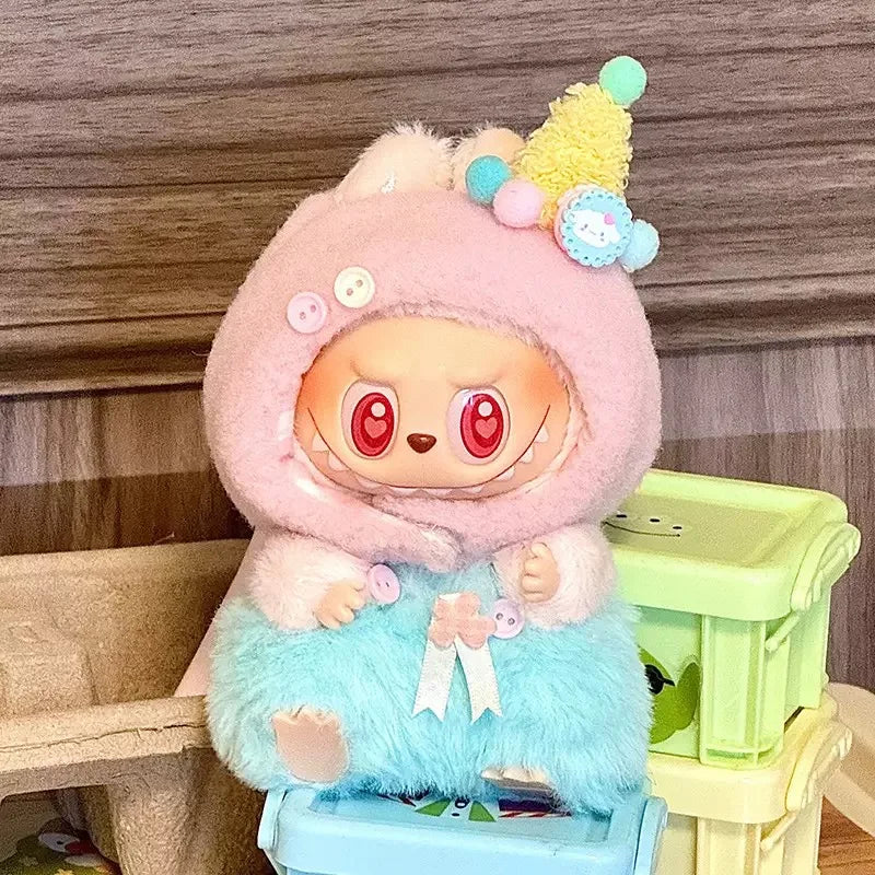 Cute plush toy with a pink hood and blue body sitting on a small stool against a wooden background.