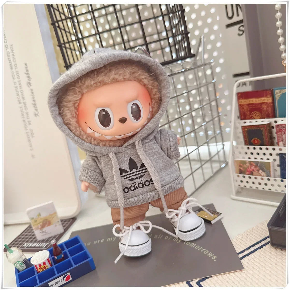 Toy figure wearing an Adidas hoodie on a desk with books and stationery items.