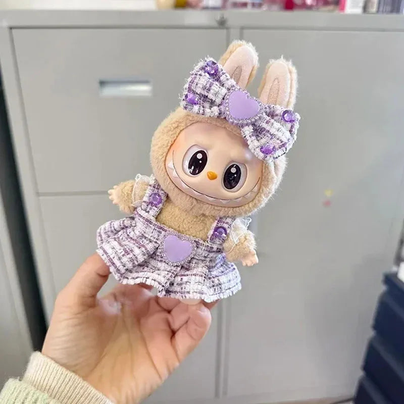 Plush toy with a purple bow and dress held in a hand against a neutral background
