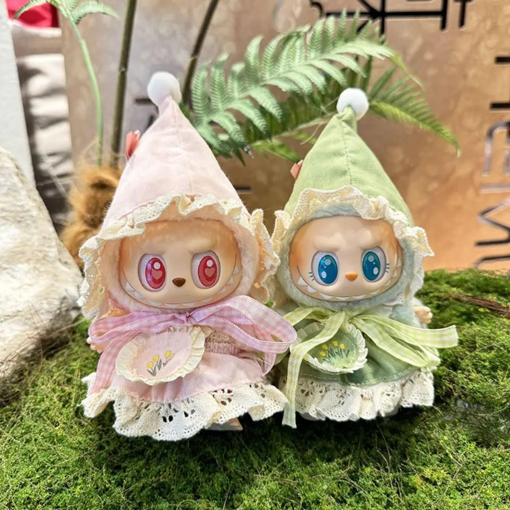 Two small plush toys with hooded dresses on a grassy surface.