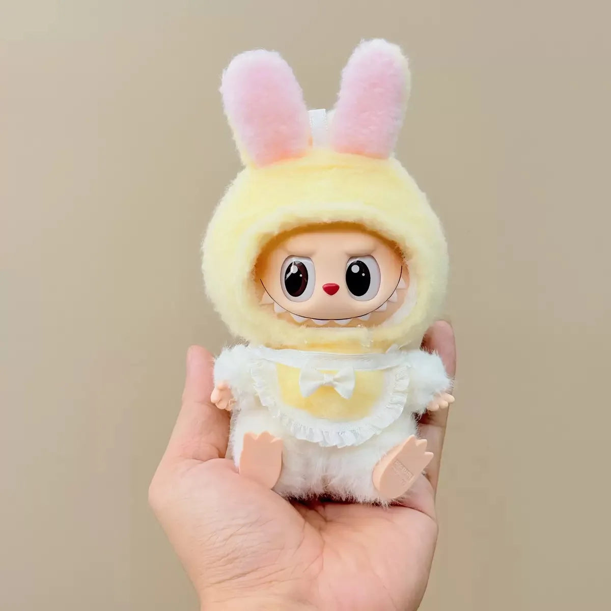 Plush toy with bunny ears held in a hand against a beige background