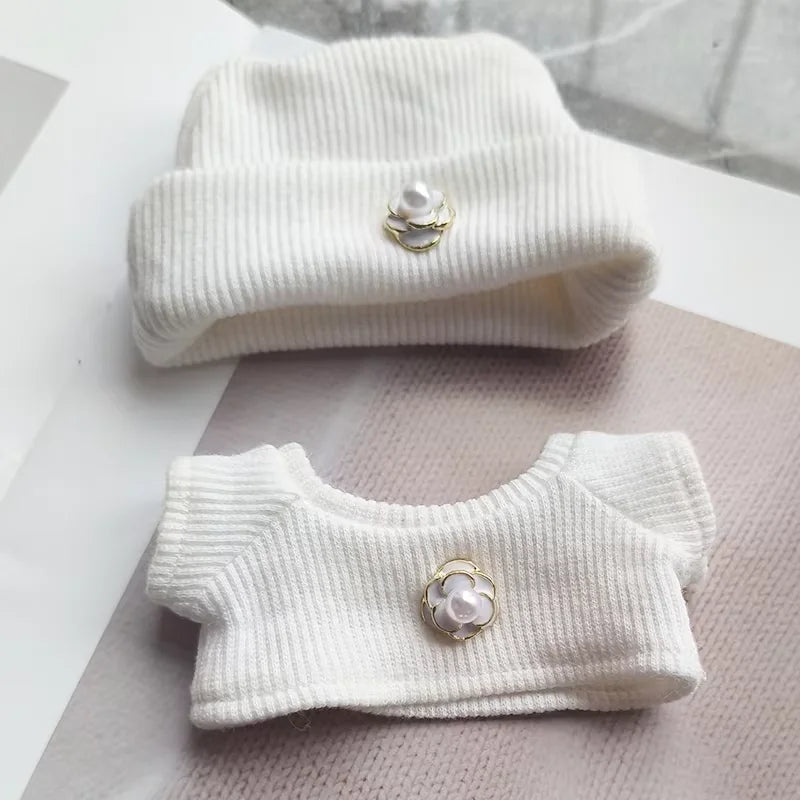 Two white ribbed knit cardigans with pearl button details on a light gray surface.