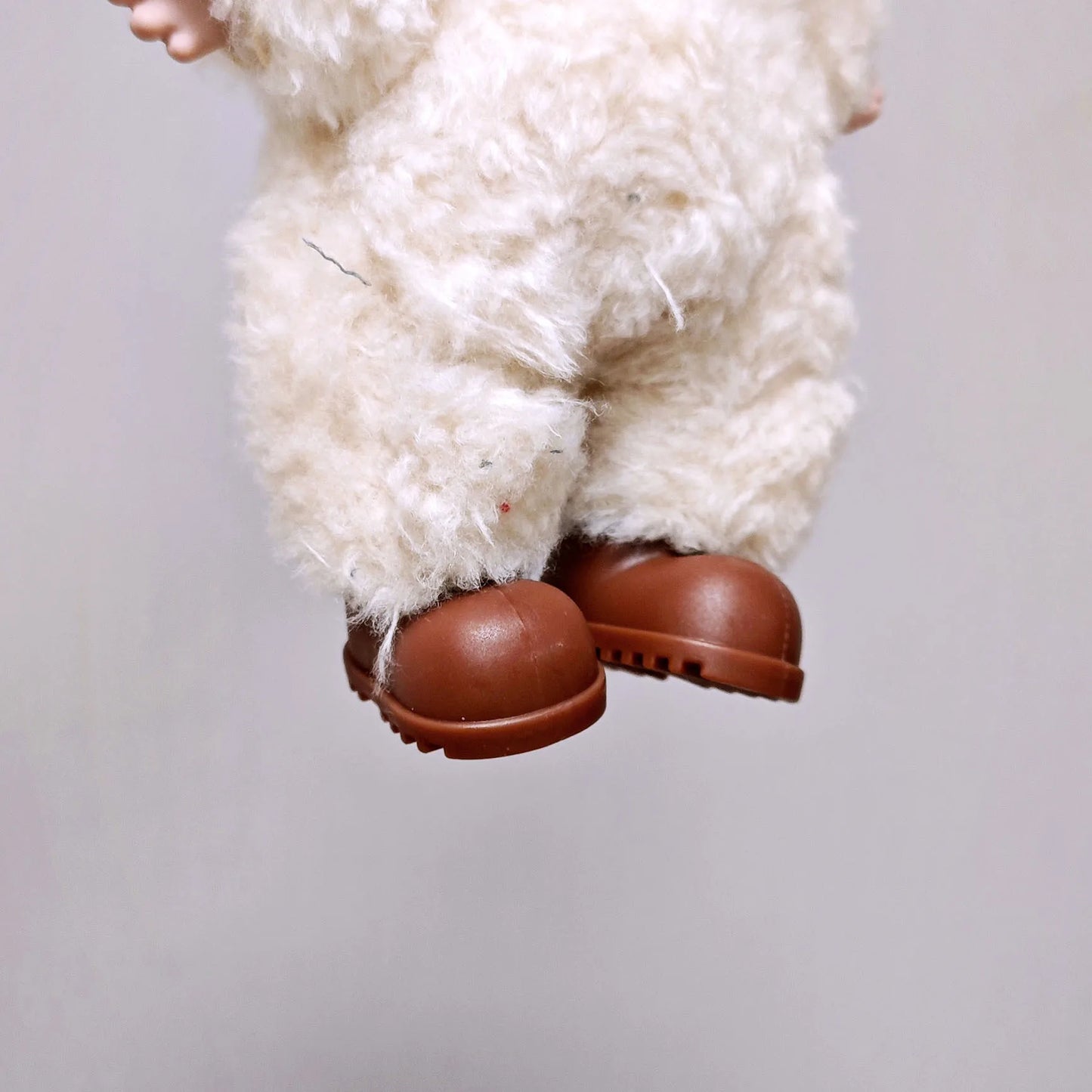 Close-up of a fluffy white creature with brown shoes on a plain background
