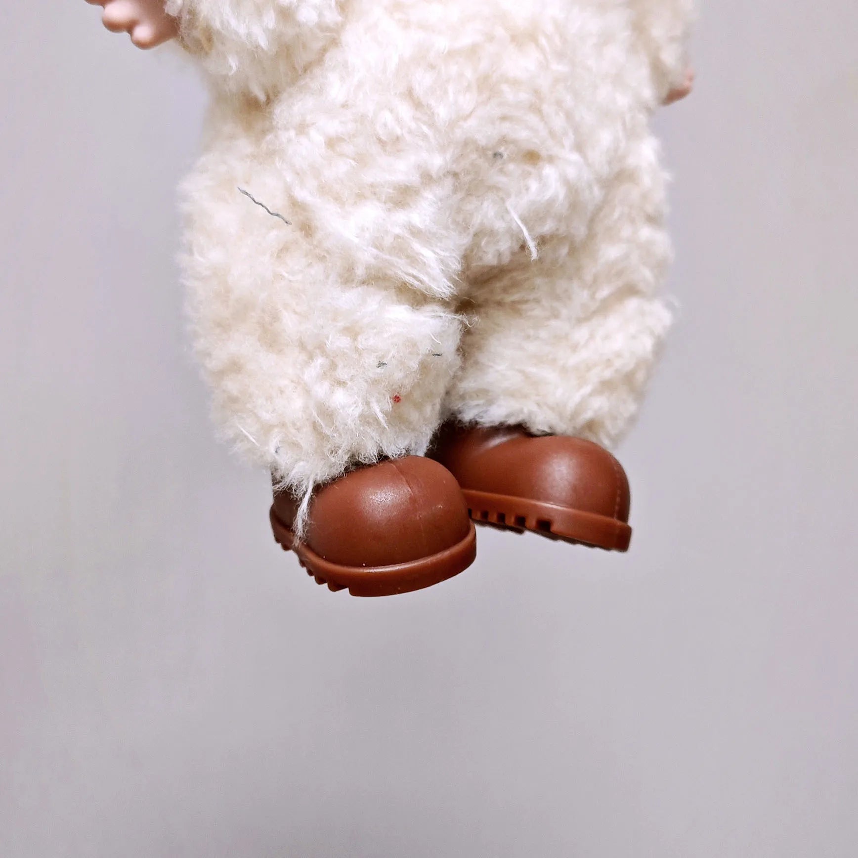 Close-up of a fluffy white creature with brown shoes on a plain background
