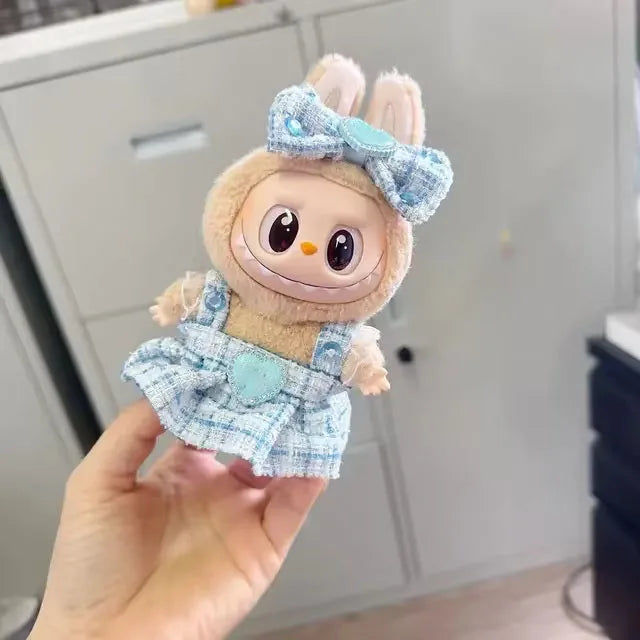 Plush toy with a blue bow and dress held by a hand against a neutral background