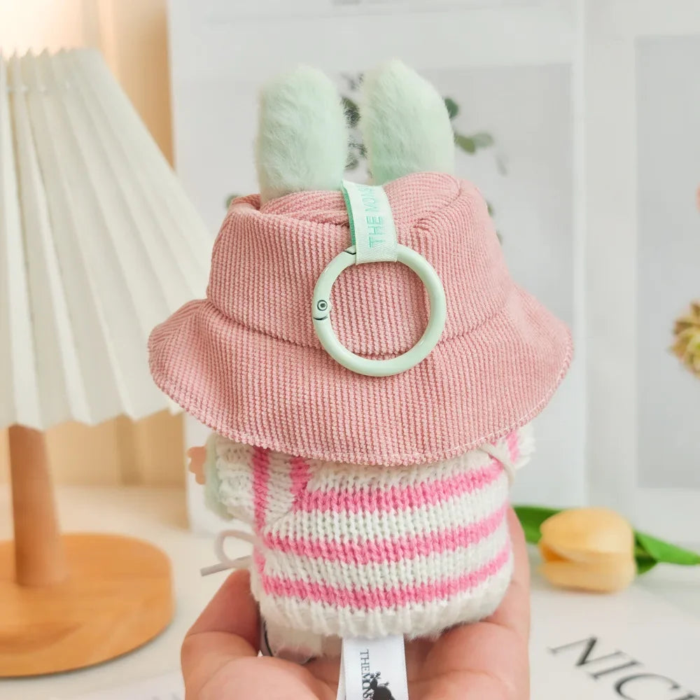 Small plush toy with a pink hat and striped body held in a hand against a blurred background.
