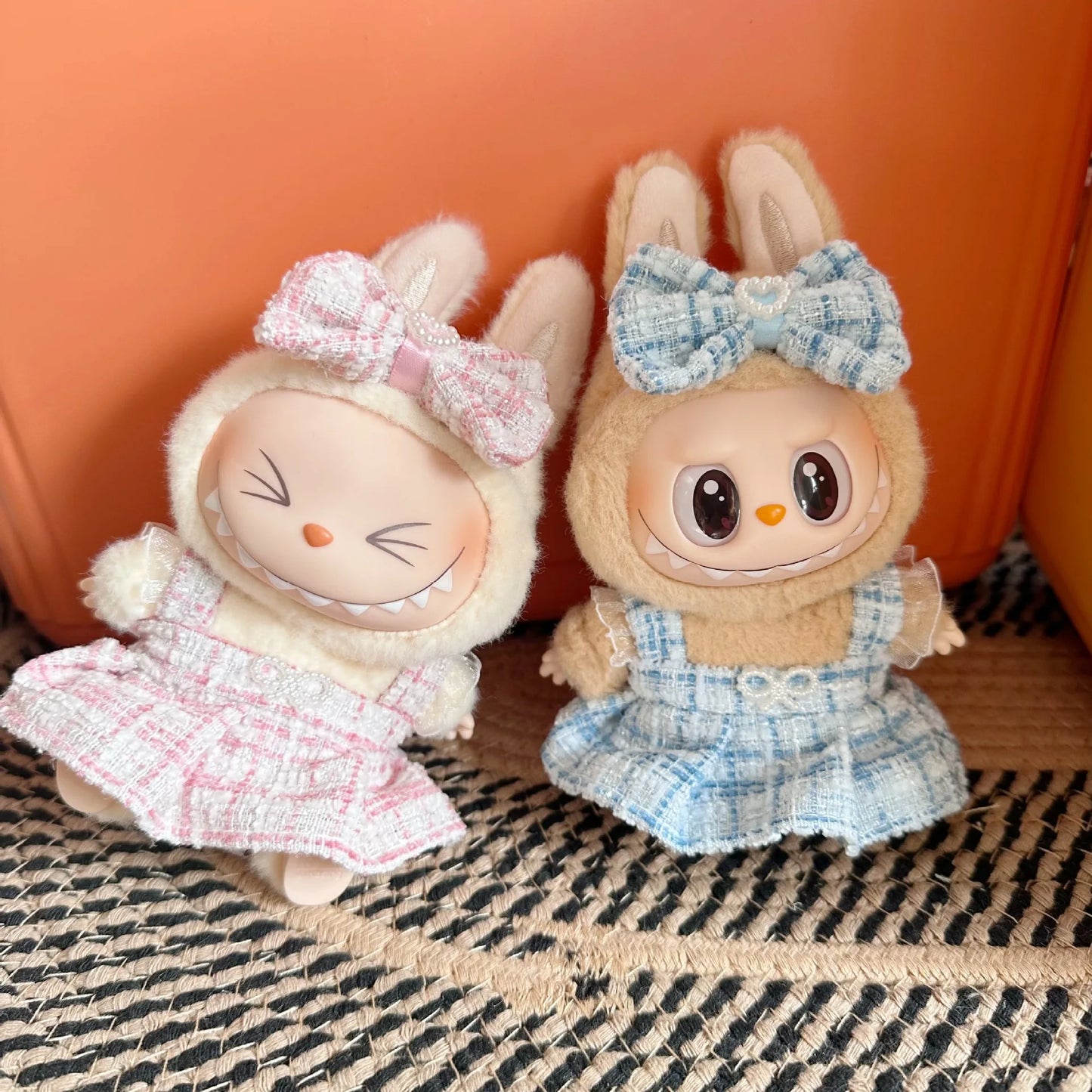 Two plush toys resembling bunnies with bows on their heads against an orange background.