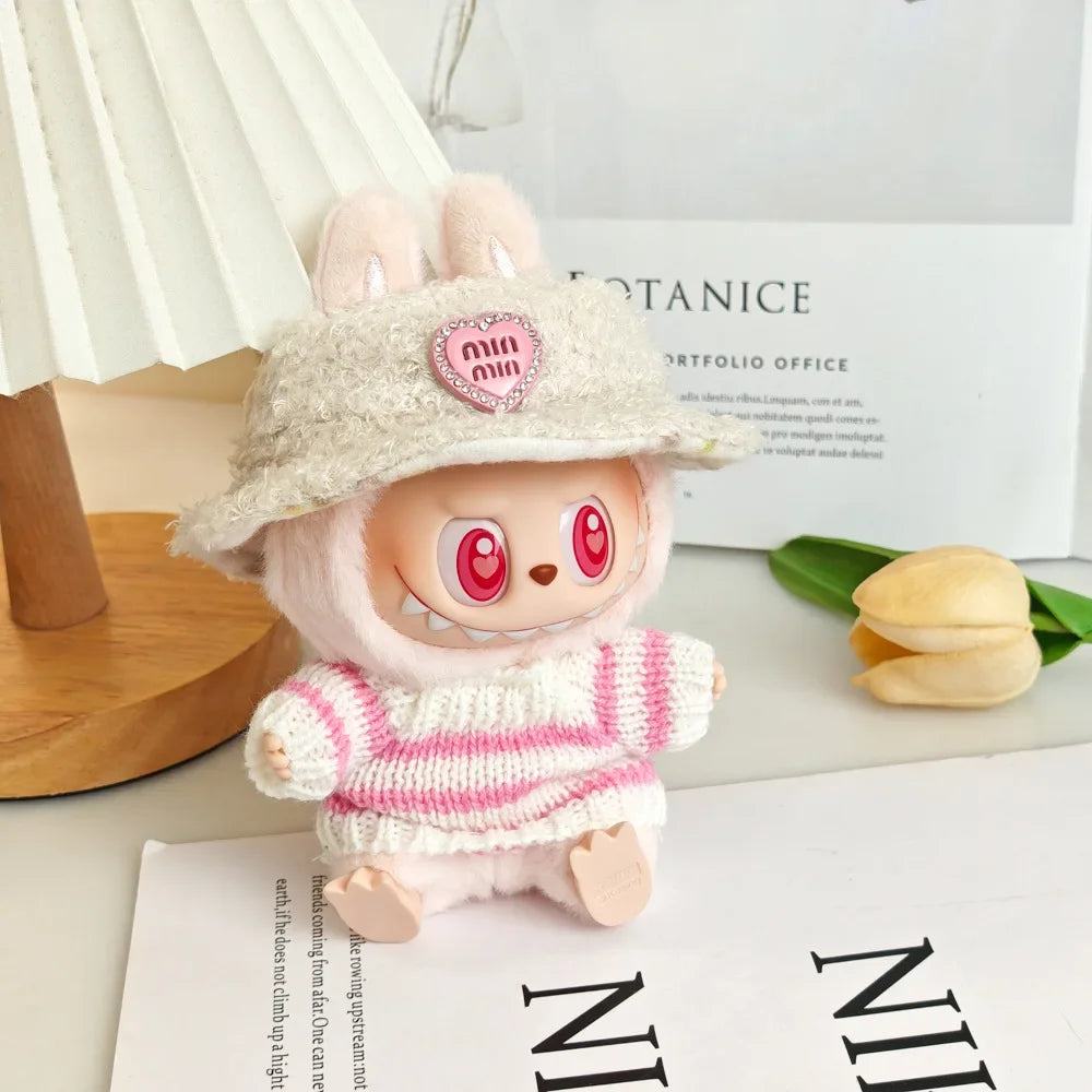 Small plush toy with bunny ears and a striped sweater on a surface with a blurred background