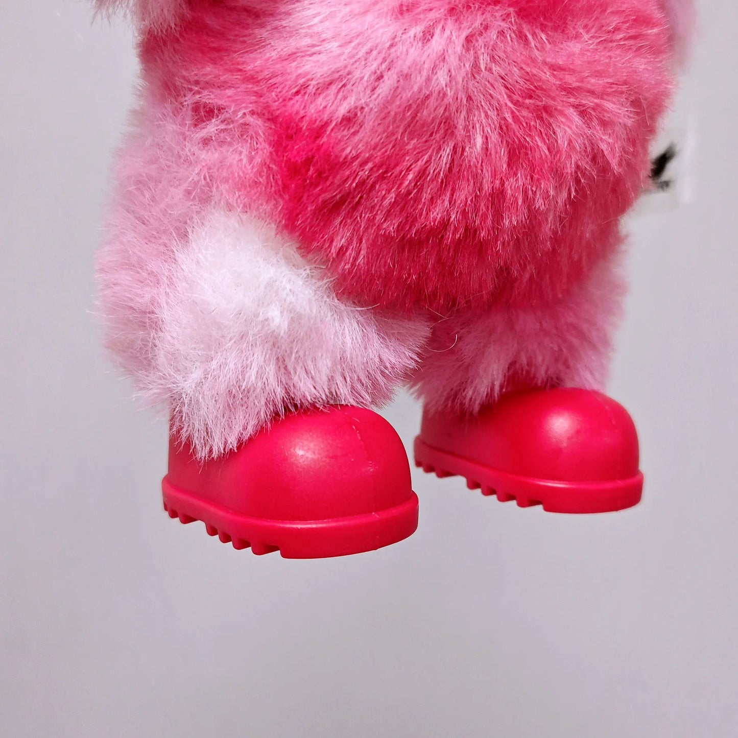 Close-up of a pink plush toy with red shoes on a light gray background
