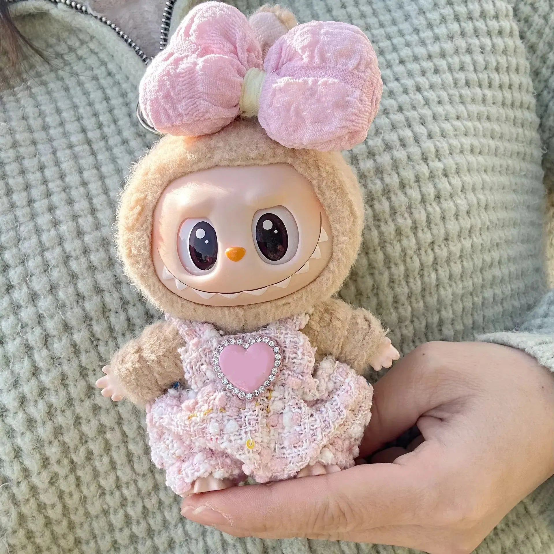 Toy figure with a pink bow and heart, held in a hand against a textured background