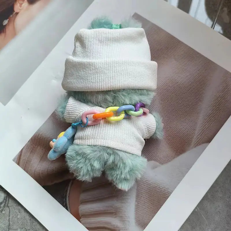Small plush toy with a white beanie and colorful chain on a wooden surface