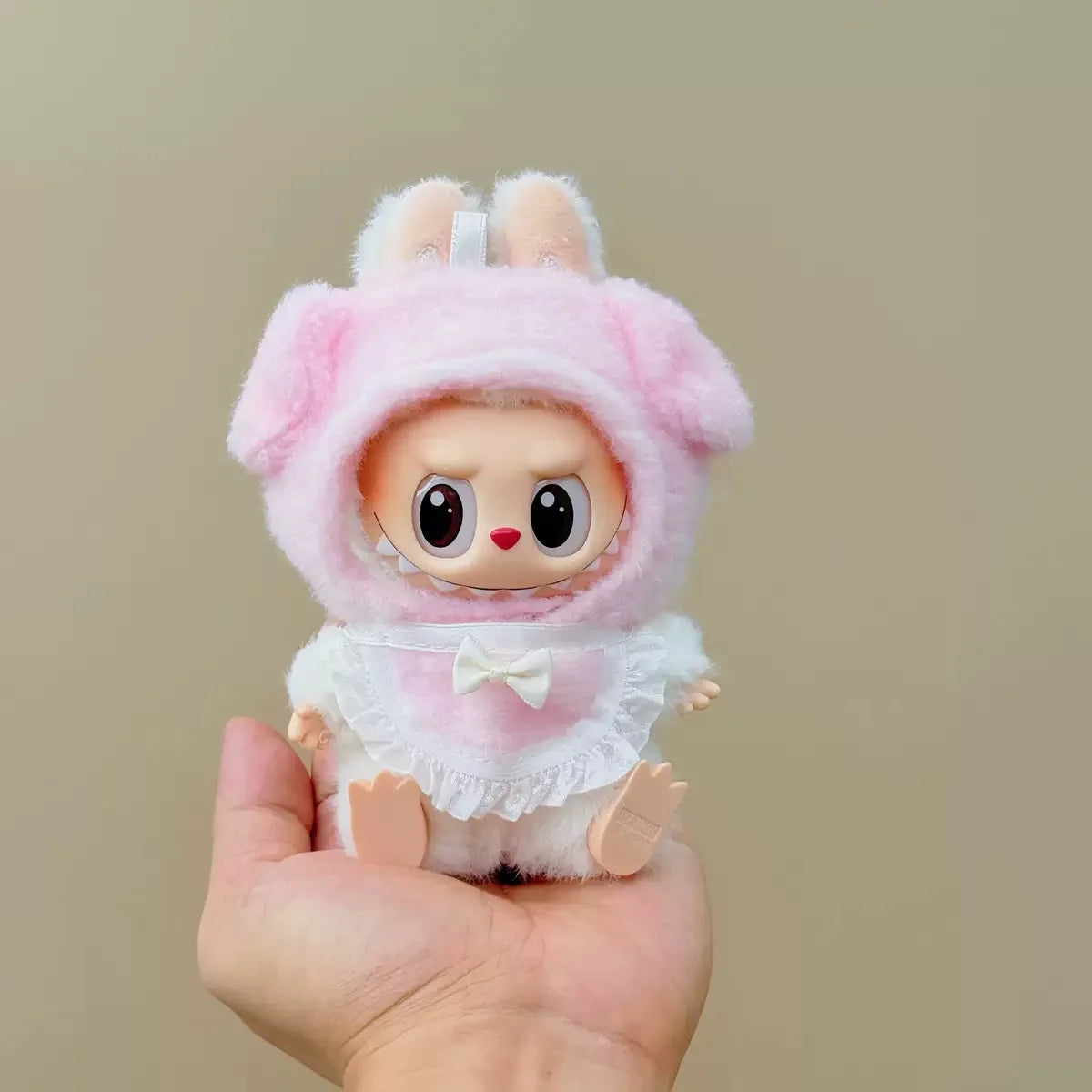 Toy figure in a pink bunny costume held in a hand against a beige background