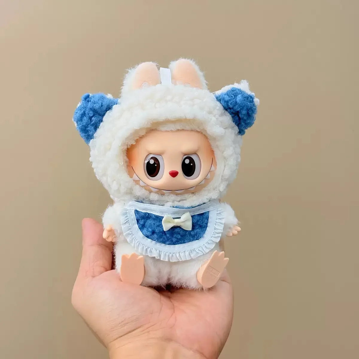 Small plush toy with a white outfit and blue accents held in a hand against a beige background