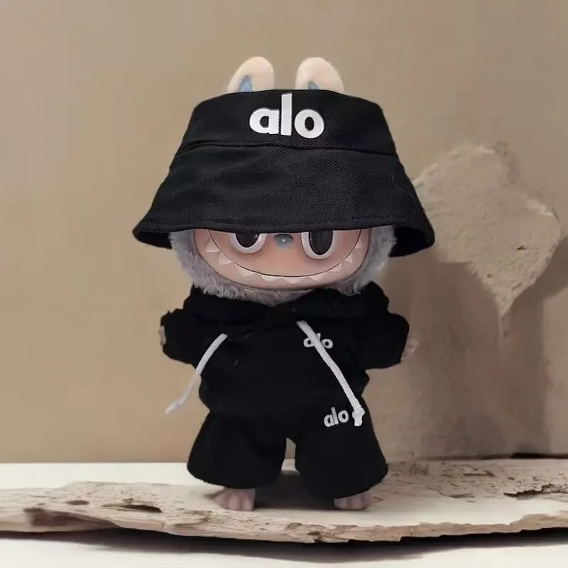 Small plush toy wearing a black 'alo' hat and outfit on a textured surface.