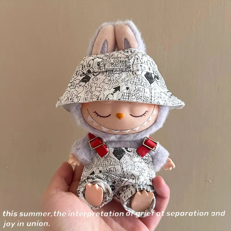Small plush toy with a patterned hat and bib held in a hand against a plain background