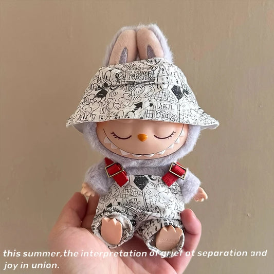 Small plush toy with a patterned hat and bib held in a hand against a plain background