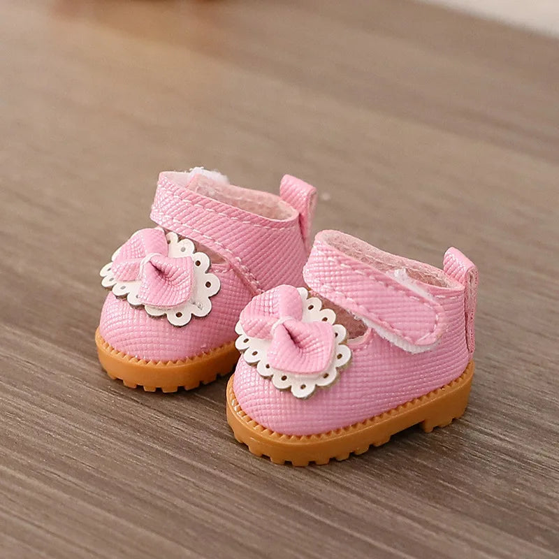 Pair of pink baby shoes with white bows on a wooden surface