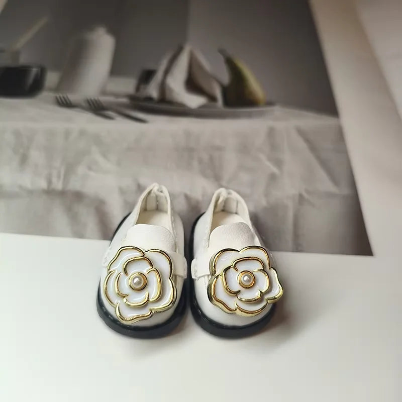 White loafers with gold flower designs on a neutral background