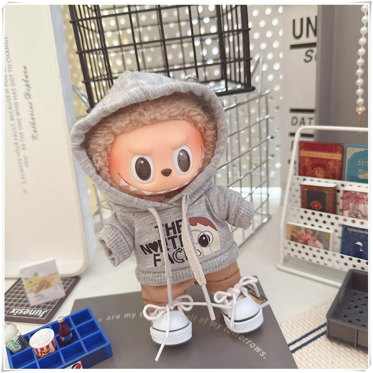 Toy figure in a gray hoodie with text, standing on a surface with a magazine rack in the background.