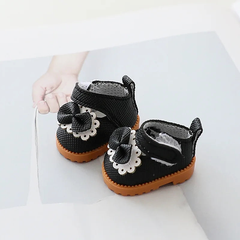 Black baby shoes with white bows held by a hand on a light background