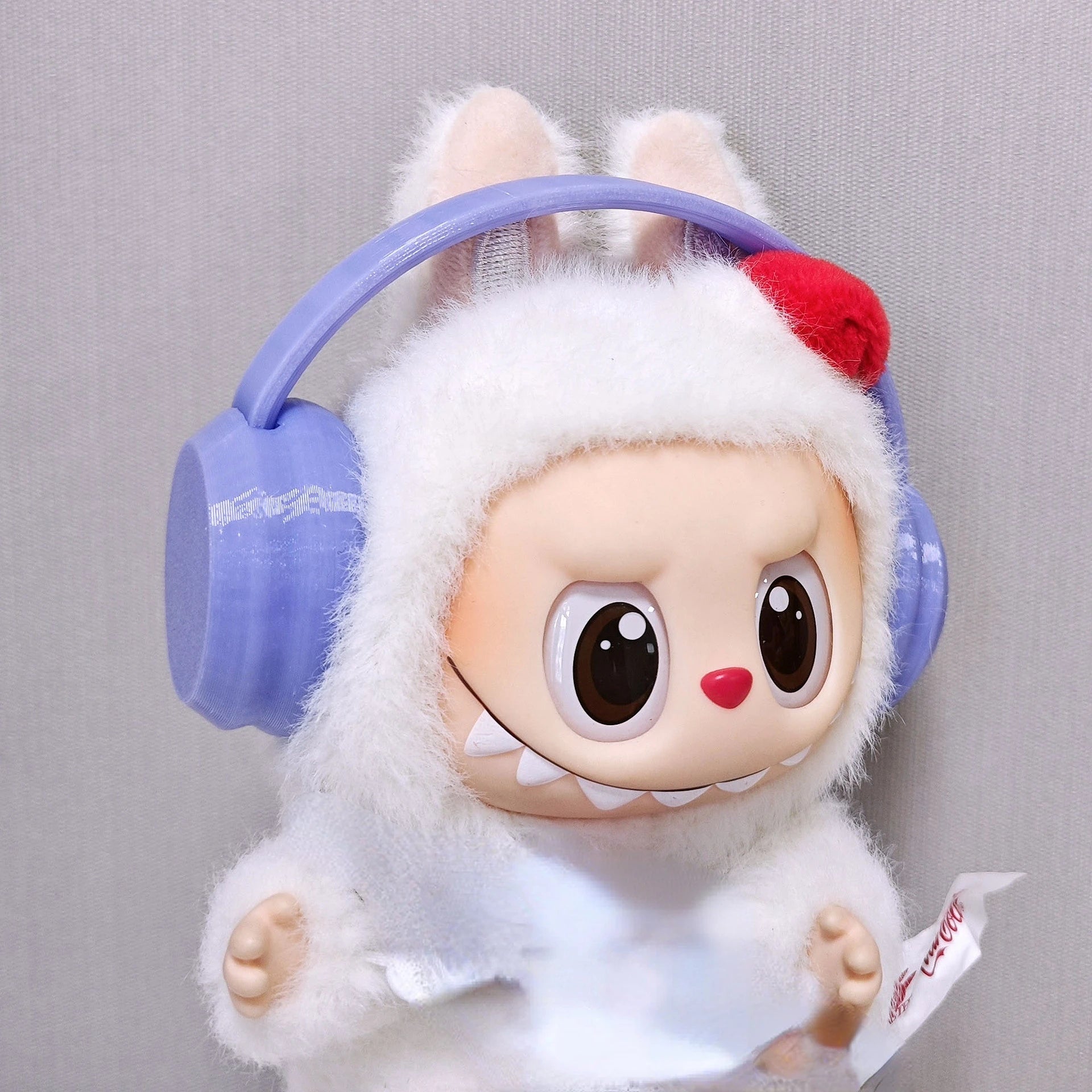 Toy figure with white fur, purple headphones, and a red flower on a gray background
