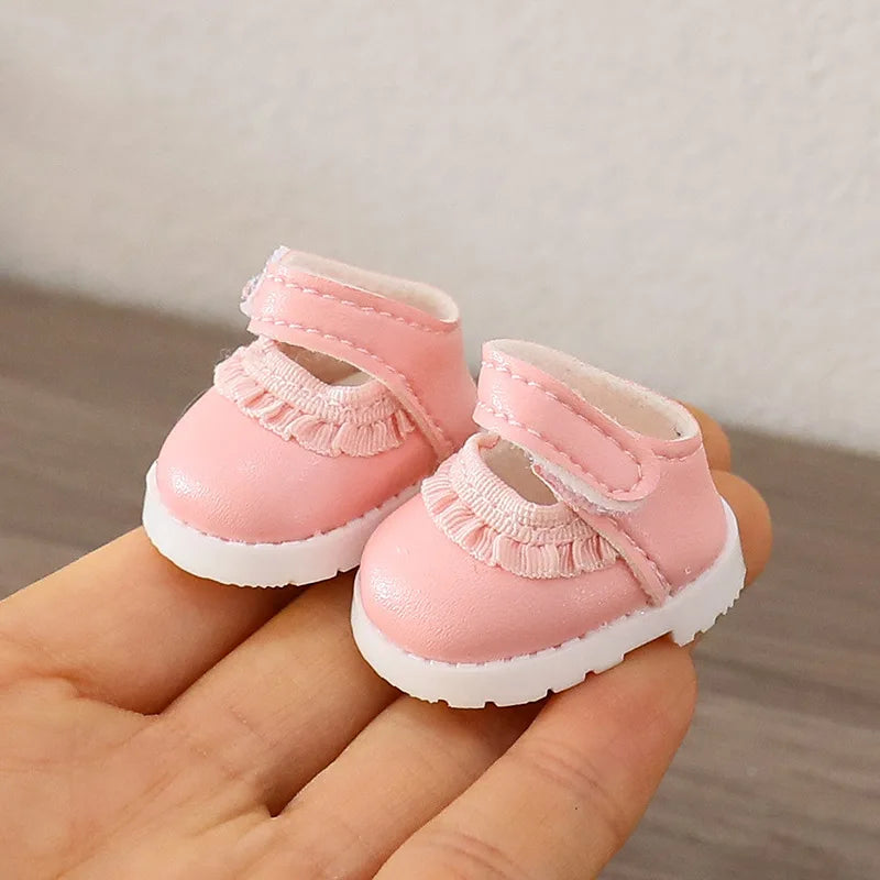 Small pink shoes held in a hand against a neutral background
