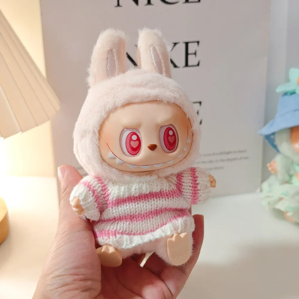 Toy figure with bunny ears and striped sweater held in a hand, with a blurred background.