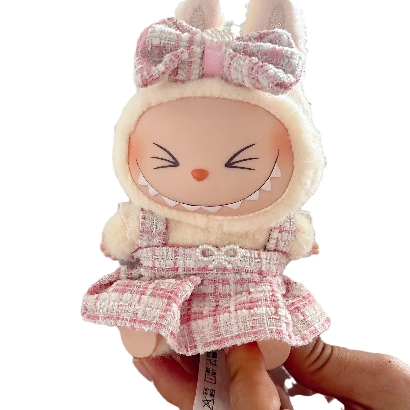 Small doll with bunny ears and a checkered dress held by a hand on a white background