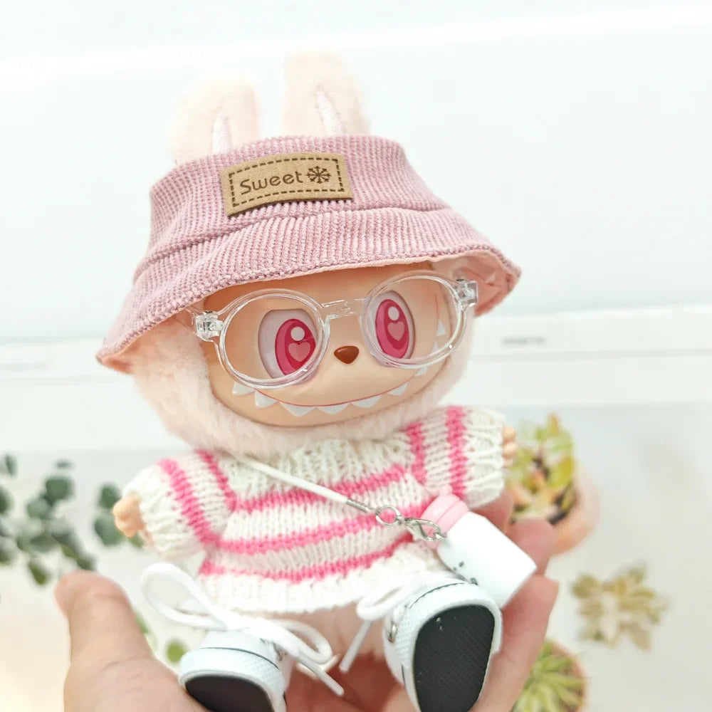 Toy figure wearing a pink hat, striped sweater, and glasses held by a hand.