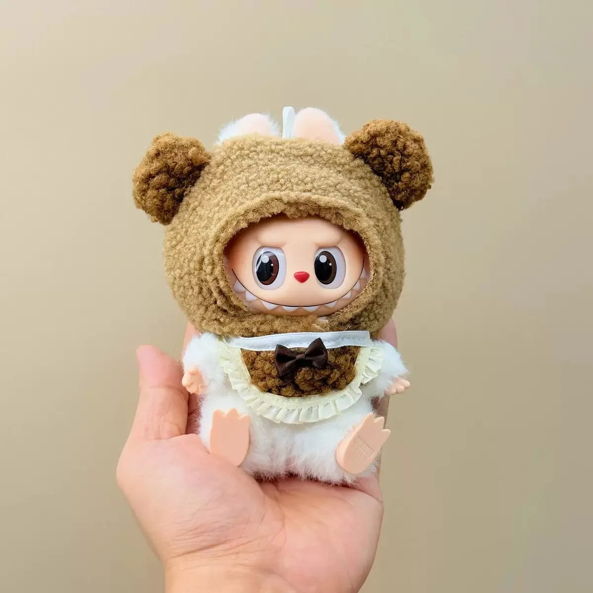 Small plush toy with a bear costume held in a hand against a beige background