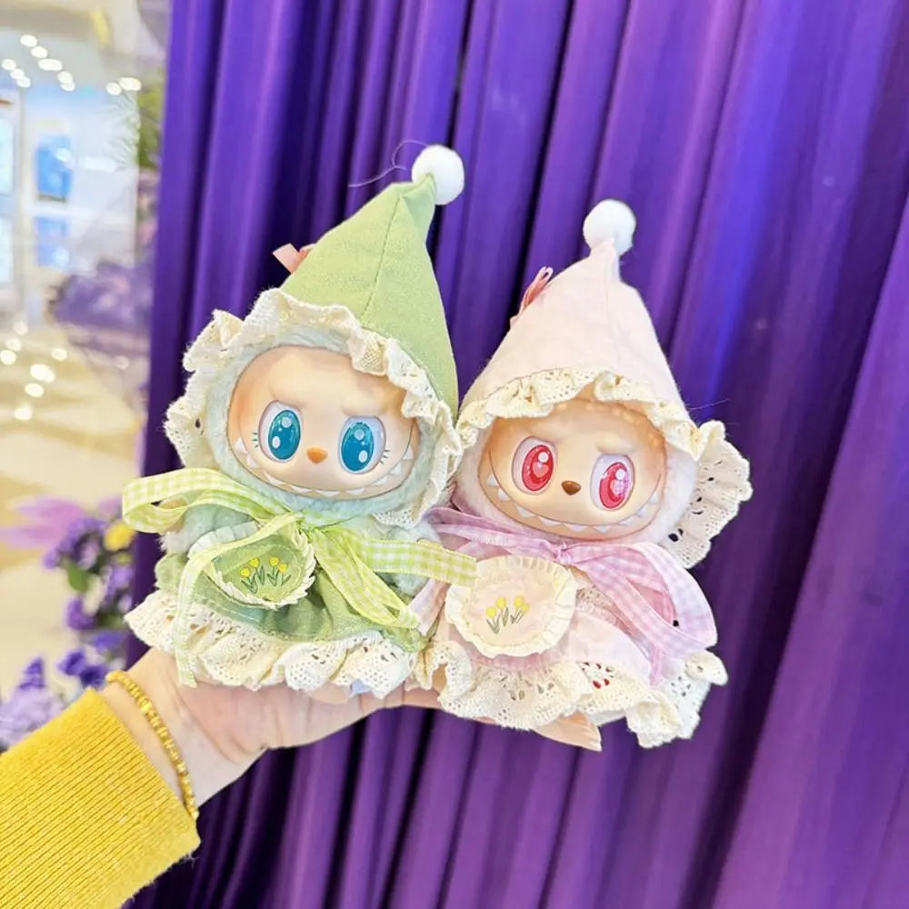 Two small plush toys with colorful dresses held against a purple curtain.