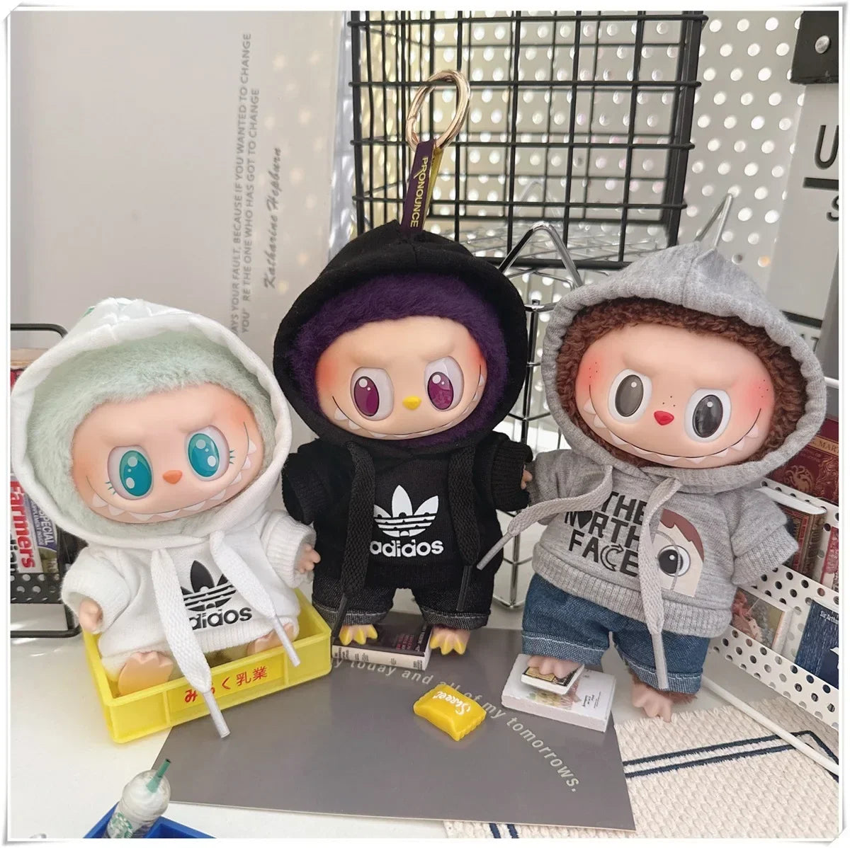 Three small dolls wearing hoodies with visible brand logos on a surface.