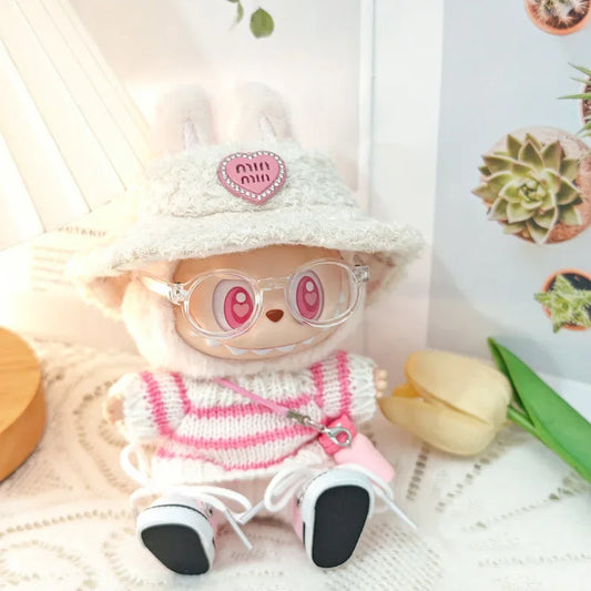 Toy figure wearing a white hat with a pink heart, pink glasses, and a striped sweater on a light background.