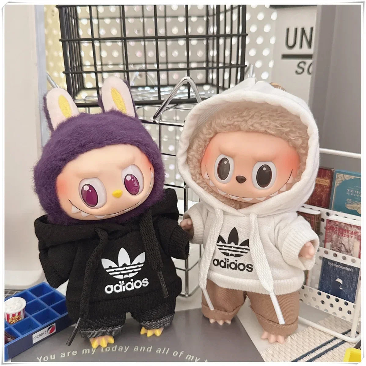 Two plush toys wearing Adidas hoodies on a surface with a blurred background