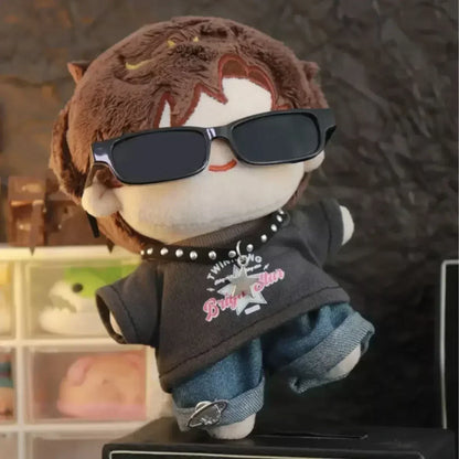Plush toy with sunglasses and a black shirt with pink text, standing on a surface with a blurred background.