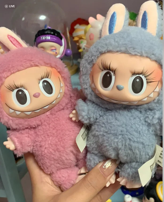 Two plush toys, one pink and one blue, held by a hand with a blurred background.