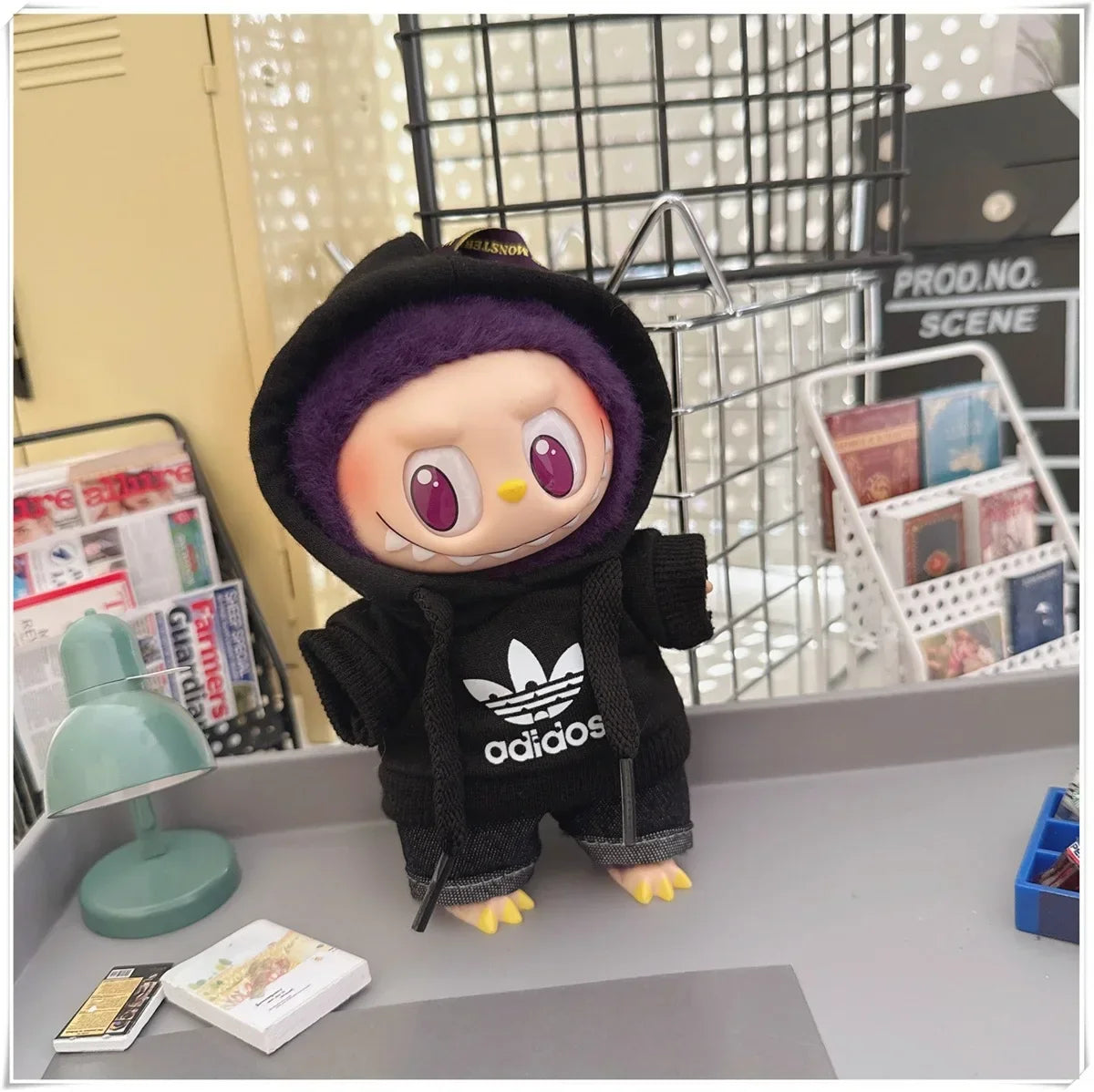 Toy figure wearing an Adidas hoodie on a desk with a magazine and lamp in the background