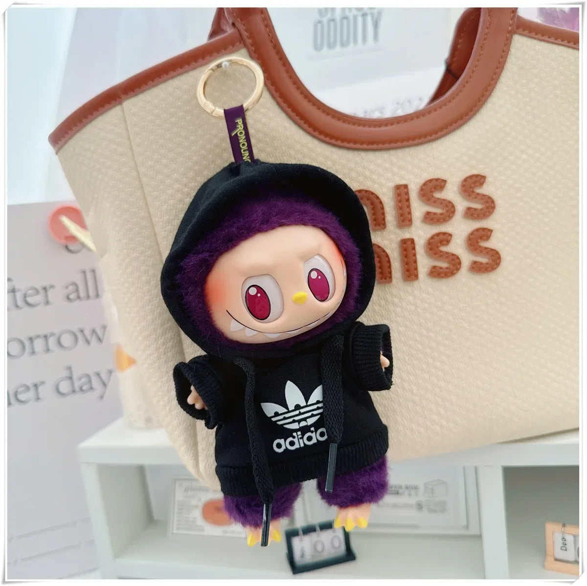 Plush keychain with a black hoodie featuring Adidas logo attached to a beige bag.