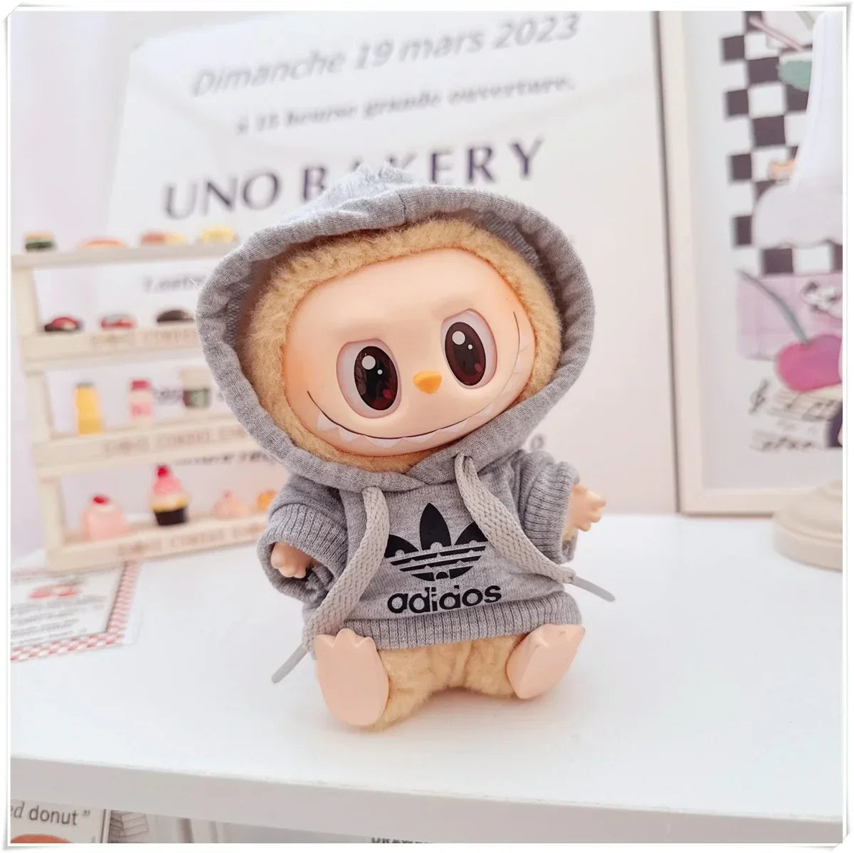 Plush toy with a hoodie featuring Adidas logo on a surface with a magazine in the background.