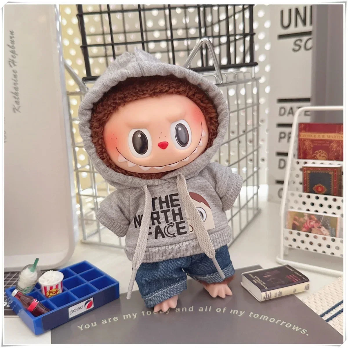Plush toy with a gray hoodie and blue pants on a surface with text