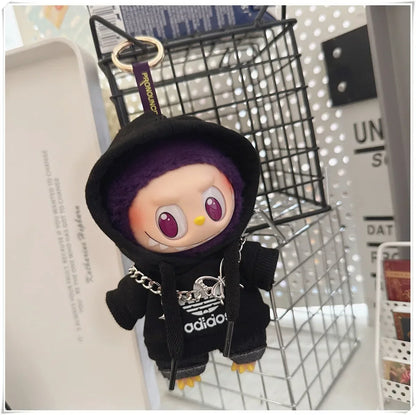 Plush toy character in a black outfit with a chain, hanging from a keychain, on a metal grid background.