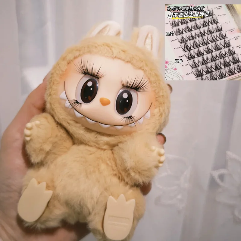 Plush toy with large eyes and a small orange beak held by a hand, with false eyelashes in the corner.
