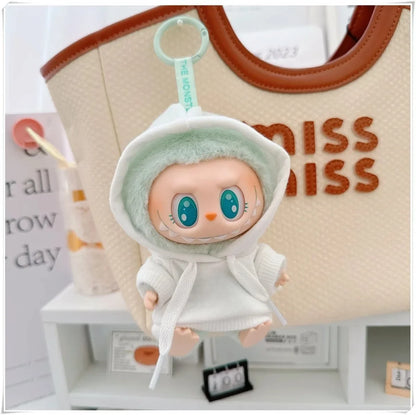 Small plush toy with a hood in front of a beige bag with 'MISS' text.