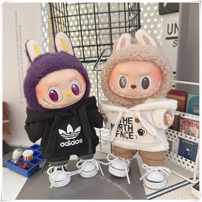 Two plush toys with animal ears, one wearing an Adidas jacket and the other wearing a North Face hoodie, on a surface with a blurred background.